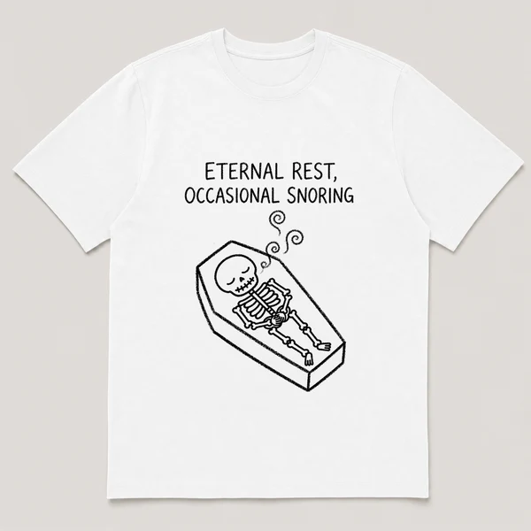 Front view of a White Tee printed with skeleton naps in a coffin with three wobbly sleep curls drifting up and the caption ETERNAL REST, OCCASIONAL SNORING