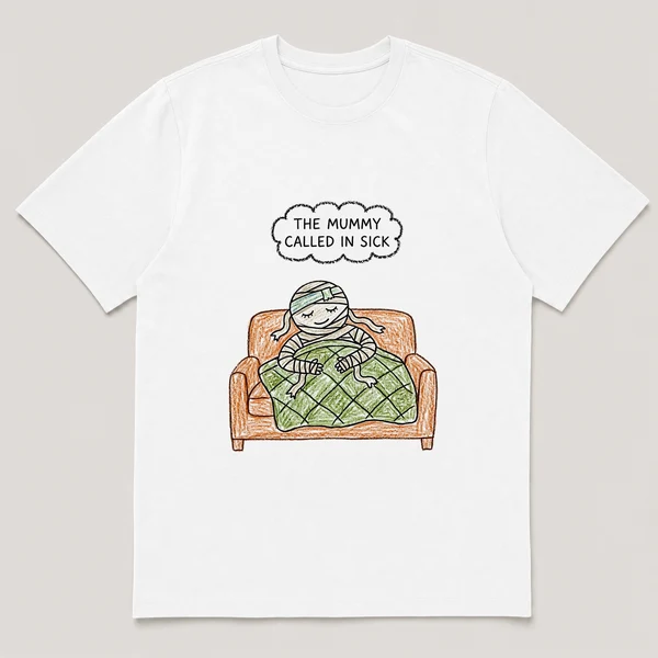 Front view of a White Tee printed with bandaged mummy naps on a couch under a quilt with a cold cloth on its head and the caption THE MUMMY CALLED IN SICK