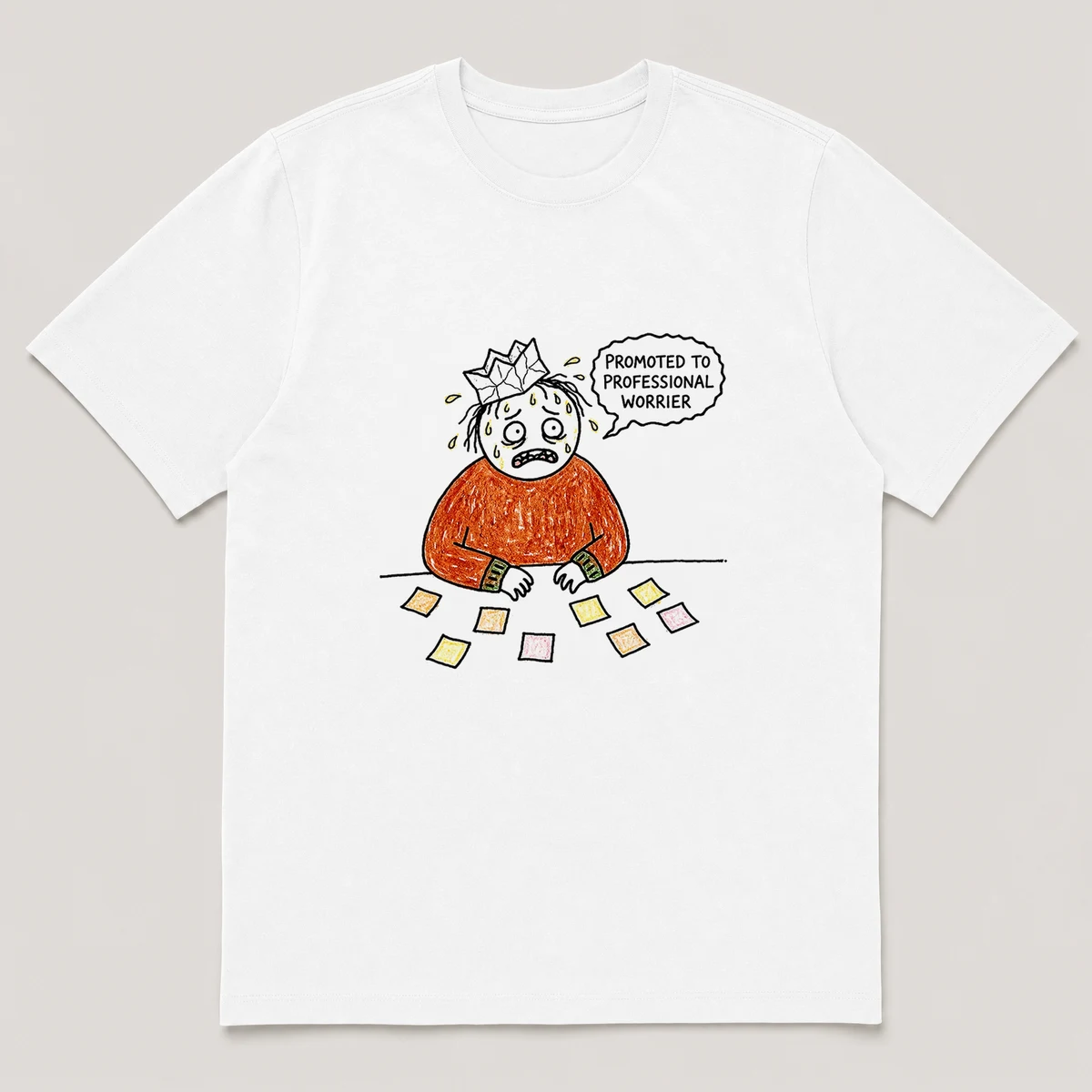 Front view of a White Tee printed with nervous guy with a crooked paper crown sweats at a desk covered in sticky notes and the caption PROMOTED TO PROFESSIONAL WORRIER